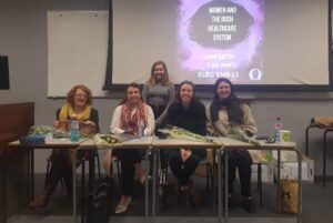 four women sitting and one standing in a classroom setting